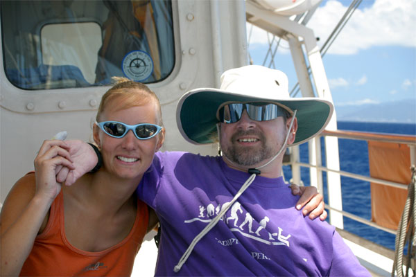 Gene and a friend wear sunglasses while smiling and posing for the camera on the sail boat on a sunny day.