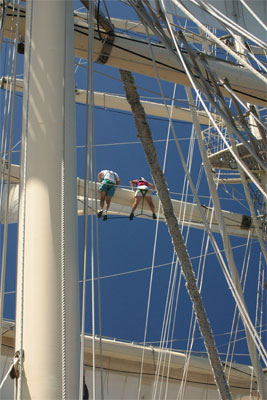 Two crew members are seen from below adjusting the sails.