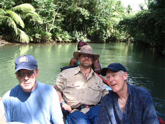 Gene and friends on a small boat on a river with lush green fields and water behind them.