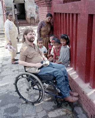 Gene sitting nin his wheelchair facing red wooden columns with Nepalese children around him