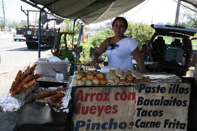 A woman smiles from her food stand featuring local Puerto Rican street food.