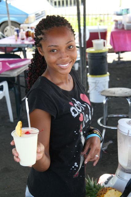 A woman extends a delicious pina colada drink with a cherry and pineapple on the rim to Gene