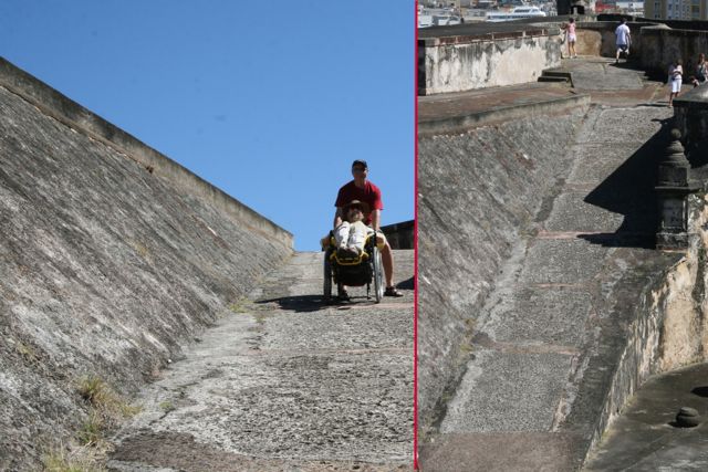 Gene in his wheel chair traversing the castle grounds on a steep hill with the help of someone.