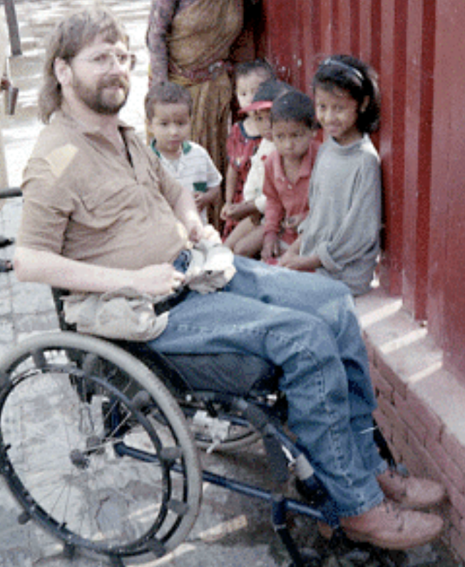 Gene seen sitting outside with two children in Peru.