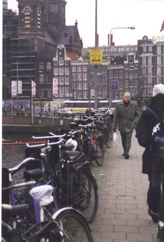 A group of people walking down the street in Amsterdam with a row of bikes