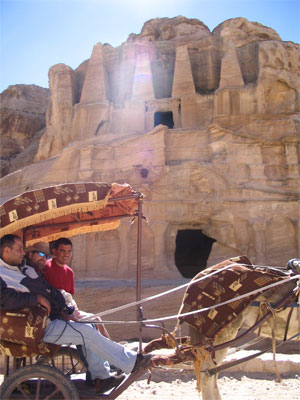 A person riding a horse drawn carriage in front of a building in Petra