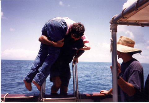 A ship crew member carrying Gene over his shoulder over the side of the ship