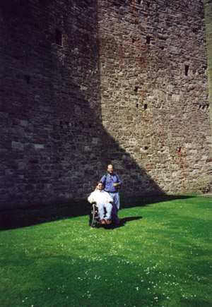 Gene and a friend pose for the camera in front of a castle's large stone walls