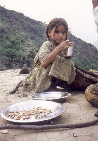 A girl squatting on the floor with a cup in her hand by a mountain in the background