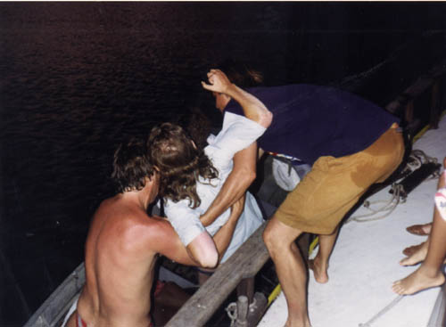 Two men lifting Gene from a rowboat.