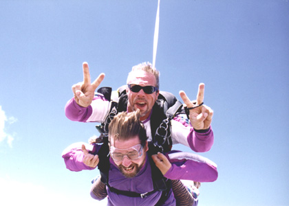 Gene tandem sky diving with his instructor giving two peace signs 