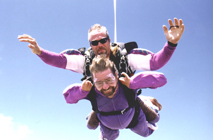Gene tandem skydiving smiling at the camera up high in the air