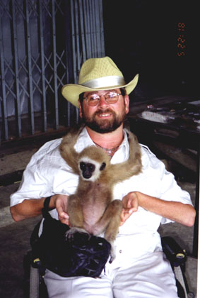 Gene smiling with a happy monkey holding his shoulders looking at the camera.