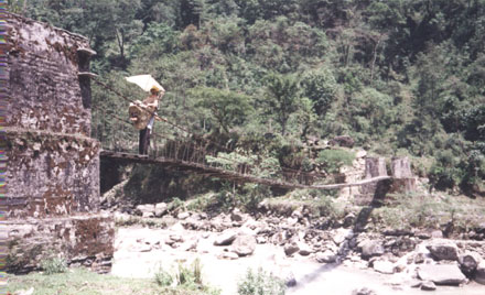 A man with a carrier on his back crossing a bridge