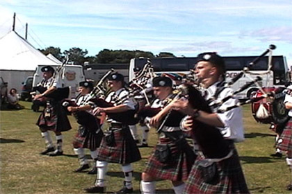 Bag pipers lines up across a field playing music