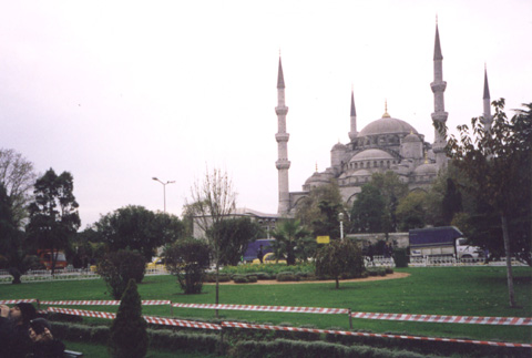 A large green field with trees in the background with Sultan Ahmed Mosque in the background