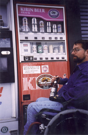 A man in a wheelchair sitting in front of a vending machine holding a bottle