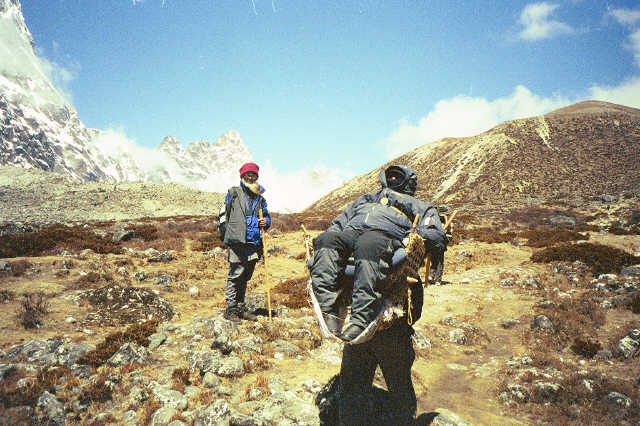 Gene being carried by a sherpa across a flat rugged terrain.
