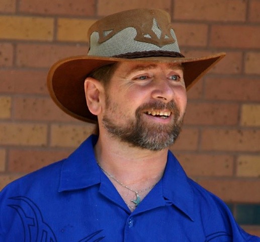 Picture of Gene smiling wearing a cowboy hat and a blue shirt. 