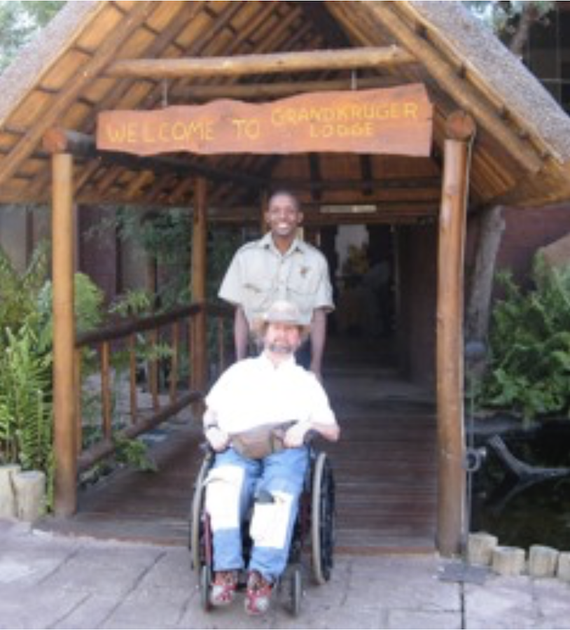 Gene in his wheel chair smiling with a guide outside of Grandkruger Lodge