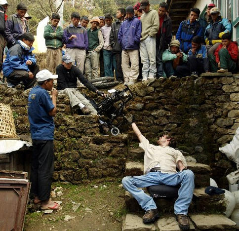 Gene and his group at the start of their adventure towards mount Everest. A man is scooting down rocky steps while a group of people look on.