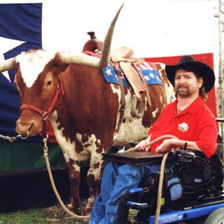 Gene outside at a fair with a large bull and the Texas flag is displayed behind them.