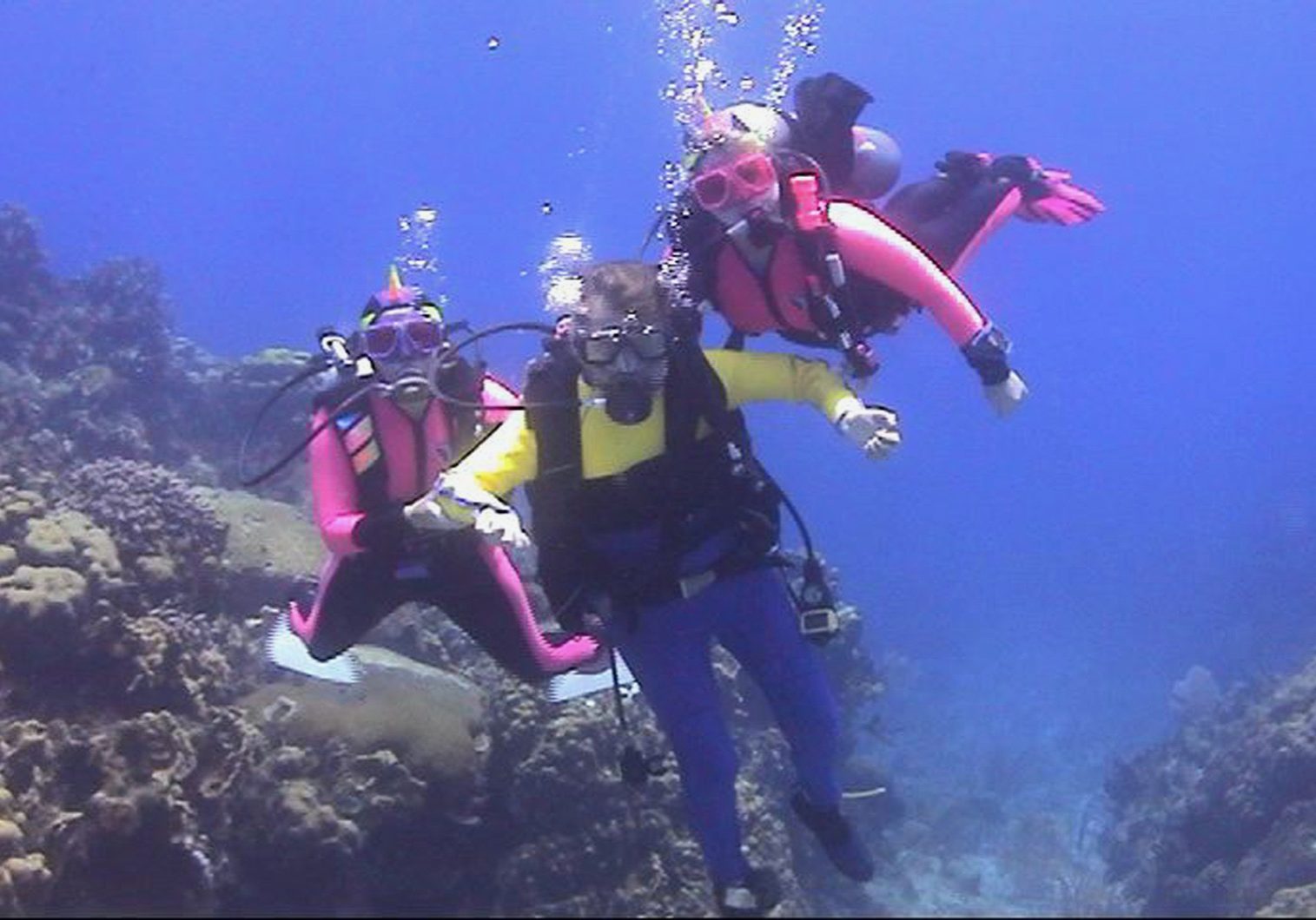 Gene in scuba gear with a dive buddy on either side of him in front of coral wall