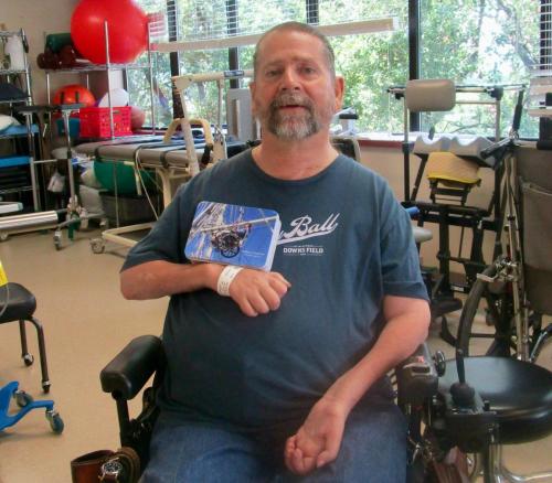 Gene holding a jigsaw puzzle that features an image of himself at St. David’s Rehab Center